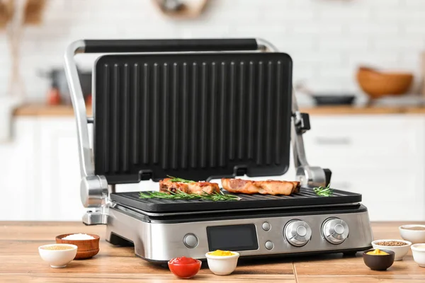Modern electric grill with tasty steaks on table in kitchen