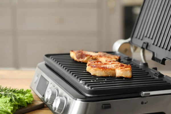 Modern electric grill with tasty steaks on table in kitchen