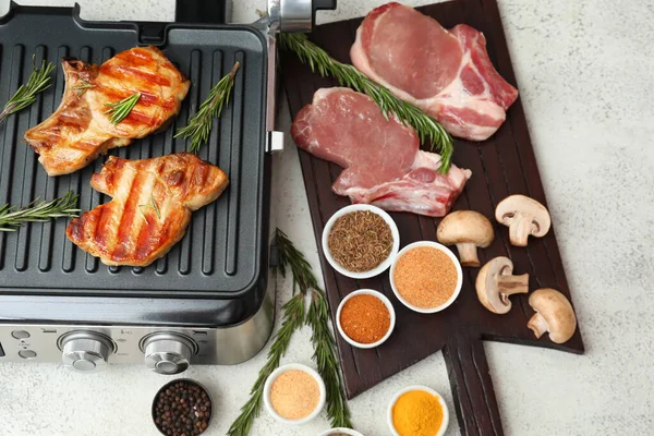 stock image Modern electric grill and board with delicious steaks on white table