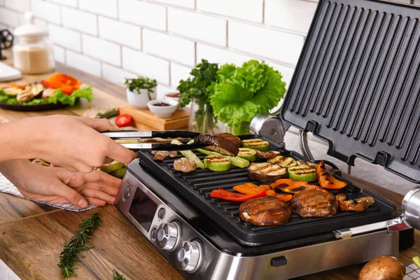 Woman cooking tasty vegetables on modern electric grill at table in kitchen