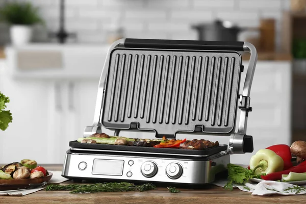 Modern electric grill with tasty vegetables on table in kitchen