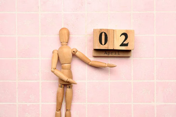 Date of World Autism Awareness Day with wooden mannequin on pink tile background
