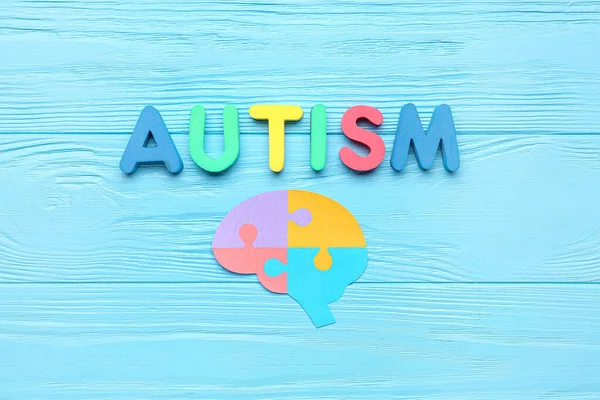 Word AUTISM with paper brain on blue wooden background