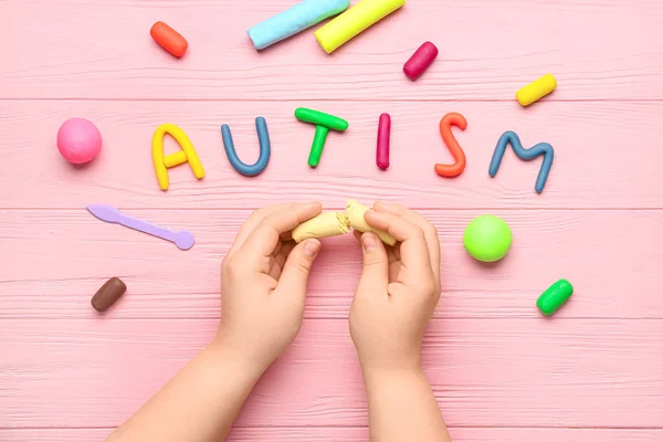 Child with plasticine and word AUTISM on pink wooden background