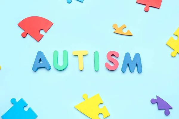 Word AUTISM with puzzle pieces on blue background
