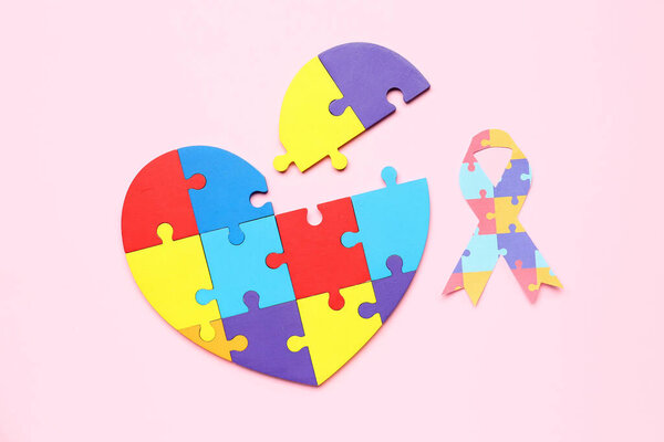 Paper ribbon with heart made of puzzle pieces on pink background. World Autism Awareness Day