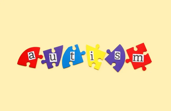 Word AUTISM with puzzle pieces on beige background
