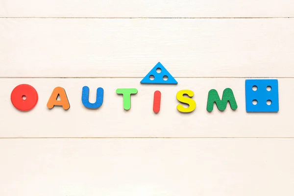 Word AUTISM with baby toys on white wooden background
