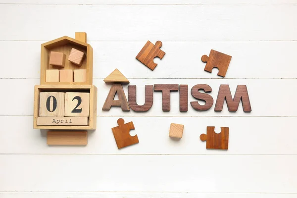 Word AUTISM with date 2 APRIL, cubes and puzzle pieces on white wooden background