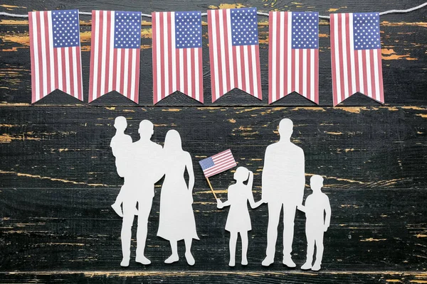 Koyu ahşap arka planda Amerikan bayrakları olan aile figürleri. Anma Günü kutlaması