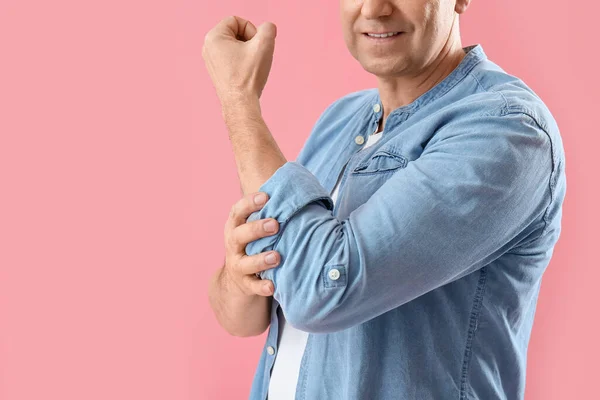 Mature man rolling up his sleeve on pink background, closeup