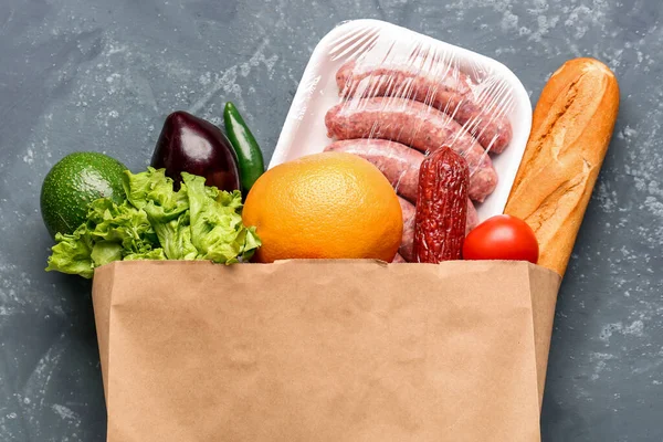 Paper bag with vegetables, sausages and bread on grey grunge background