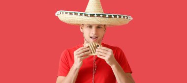 Genç Meksikalı adam kırmızı arka planda lezzetli quesadilla yiyor.