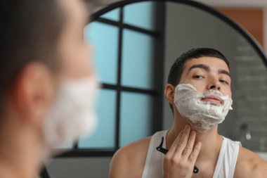 Genç adam banyoda tıraş oluyor.