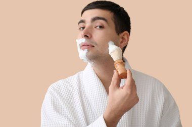 Bej arka planda tıraş olan genç bir adam.