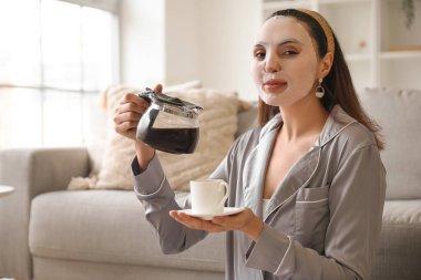 Çarşaf maskeli genç bir kadın, kahve makinesi ve fincanı evde.