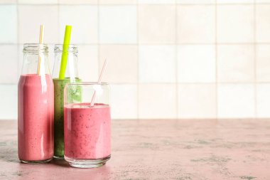 Bardak ve renkli meyve suları pembe masada.