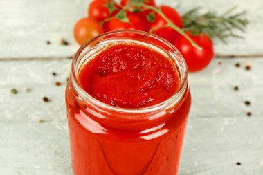 Hafif ahşap arka planda lezzetli domates ezmeli kavanoz, yakın plan.