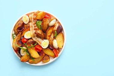 Yumurtalı, domatesli ve açık mavi arka planda domuz pastırmalı lezzetli patates salatası.