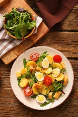 Tahta arka planda yumurta ve domatesli lezzetli patates salatası.