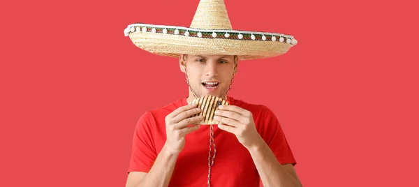Young Mexican man eating tasty quesadilla on red background