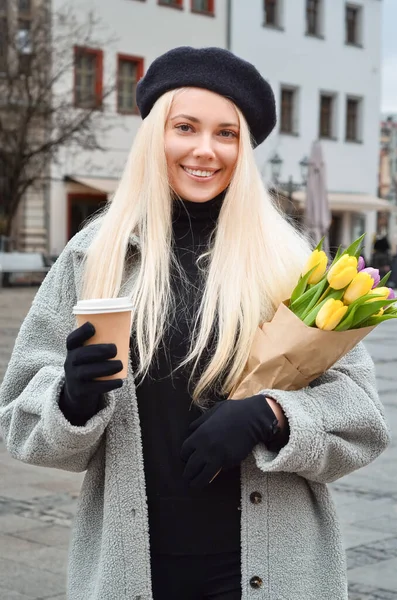 Young woman with tulips and cup of coffee on city street