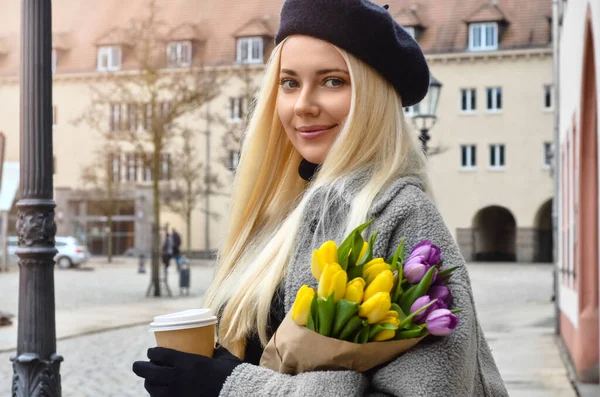 Young woman with tulips and cup of coffee on city street, closeup