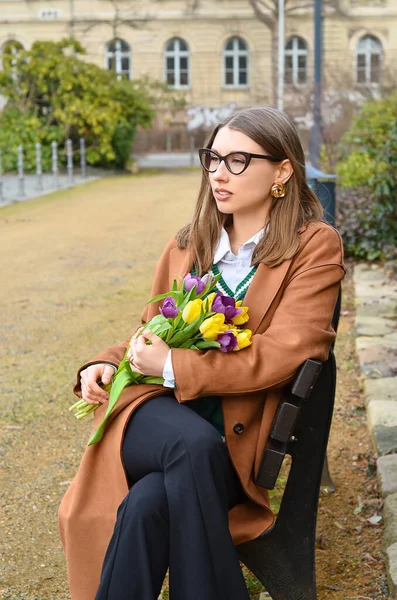 Young woman with tulips sitting on bench in park