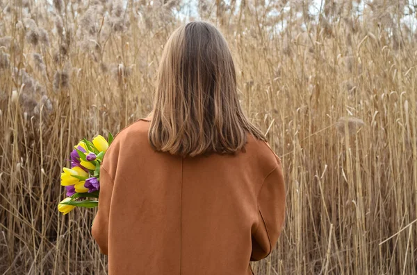 Young woman with tulips near pampas grass outdoors, back view