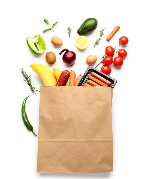 Paper bag with vegetables, fruits and sausages on white background