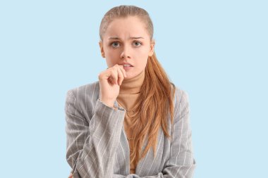 Young businesswoman biting nails on blue background