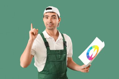 Renk paletleri olan erkek ressam yeşil arka plandaki bir şeyi işaret ediyor