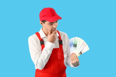 Mavi arka planda renk paletleri olan düşünceli bir erkek ressam.