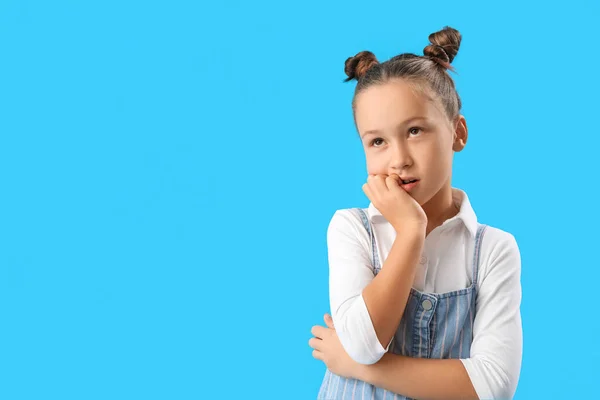 Little girl biting nails on blue background