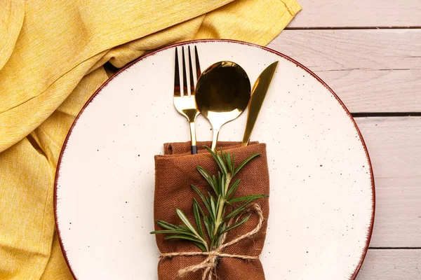 Plate with napkin, set of cutlery and rosemary on white wooden background