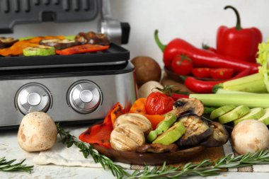 Lezzetli sebzeli tabaklar ve arka planda modern elektrikli ızgara.