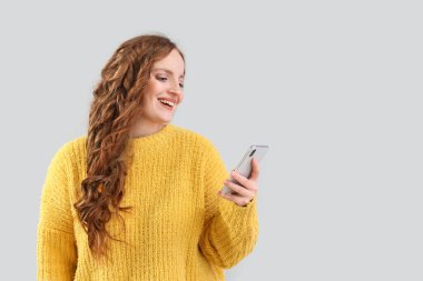 Gri arka planda cep telefonu kullanan güzel kızıl saçlı kadın.