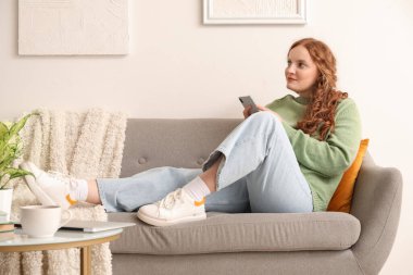 Evdeki koltukta cep telefonu kullanan güzel kızıl saçlı kadın.