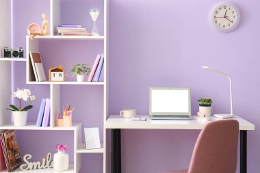 Ofiste eflatun duvarının yanında dizüstü bilgisayarı ve kırtasiyesi olan bir iş yeri.