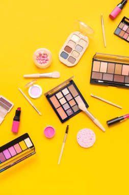 Sarı arka planda makyaj fırçası olan dekoratif kozmetik ürünler.