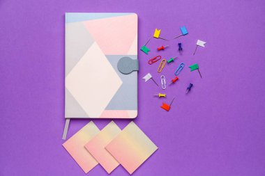 Mor arkaplanda yapışkan notlar, not defterleri ve ataçlar