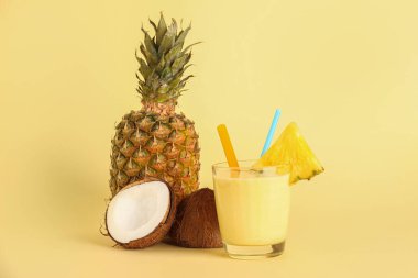 Sarı arka planda bir bardak lezzetli ananas, saman ve hindistan cevizi.