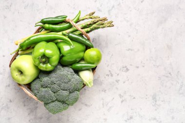 Farklı taze sebzeler ve arkaplanda meyveler olan sepet.