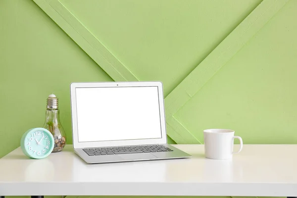 Workplace with laptop, alarm clock and cup near green wall