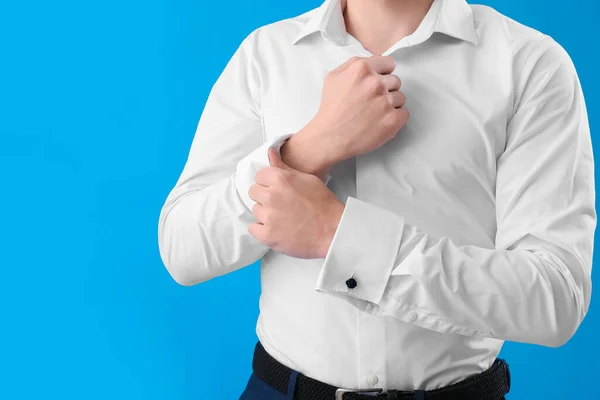 Young businessman rolling up his sleeve on light blue background, closeup