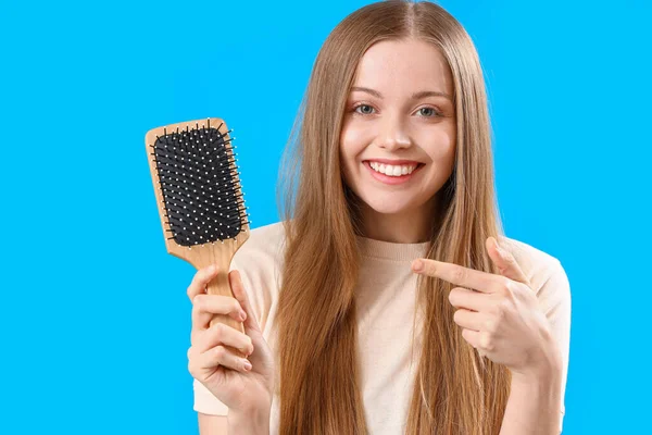 Pretty young woman with hair brush on blue background