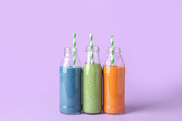 Glasflaschen Mit Verschiedenen Leckeren Smoothies Mit Strohhalmen Auf Violettem Hintergrund — Stockfoto
