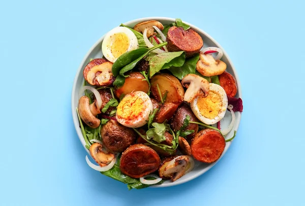 Plate of tasty potato salad with eggs and mushrooms on light blue background, top view