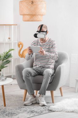 Young man with VR glasses and tablet computer at home