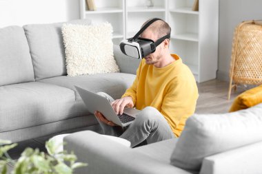 Evde VR gözlük ve laptop kullanan genç adam.